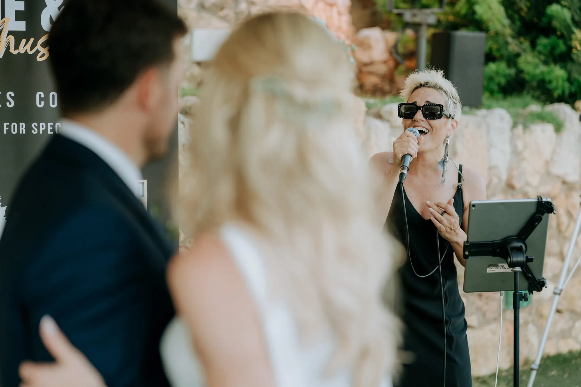 Chloe Ly cantando con micrófono frente a una pareja de novios durante su ceremonia al aire libre