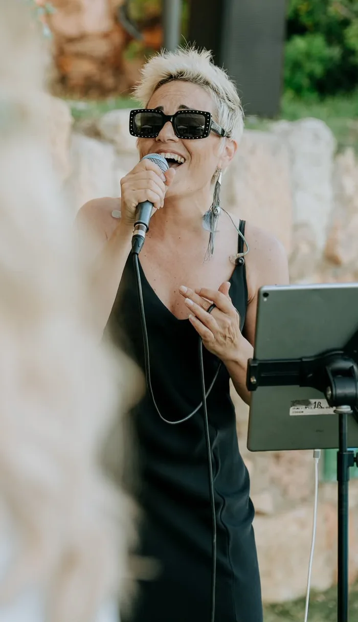Chloe Ly cantando al micrófono con gafas de sol en una ceremonia al aire libre